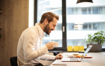 Mann mit Kaffeetaste in der Hand vor einem Laptop