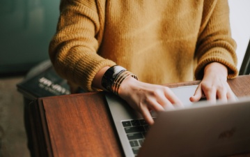 Person in gelben Pullover bedient einen Laptop.