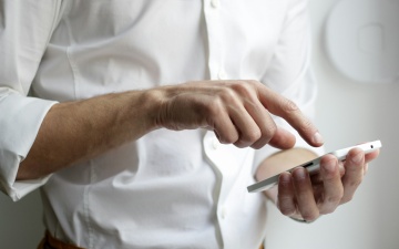 Eine Person in weißem Hemd hält ein weißes Smartphone in den Händen